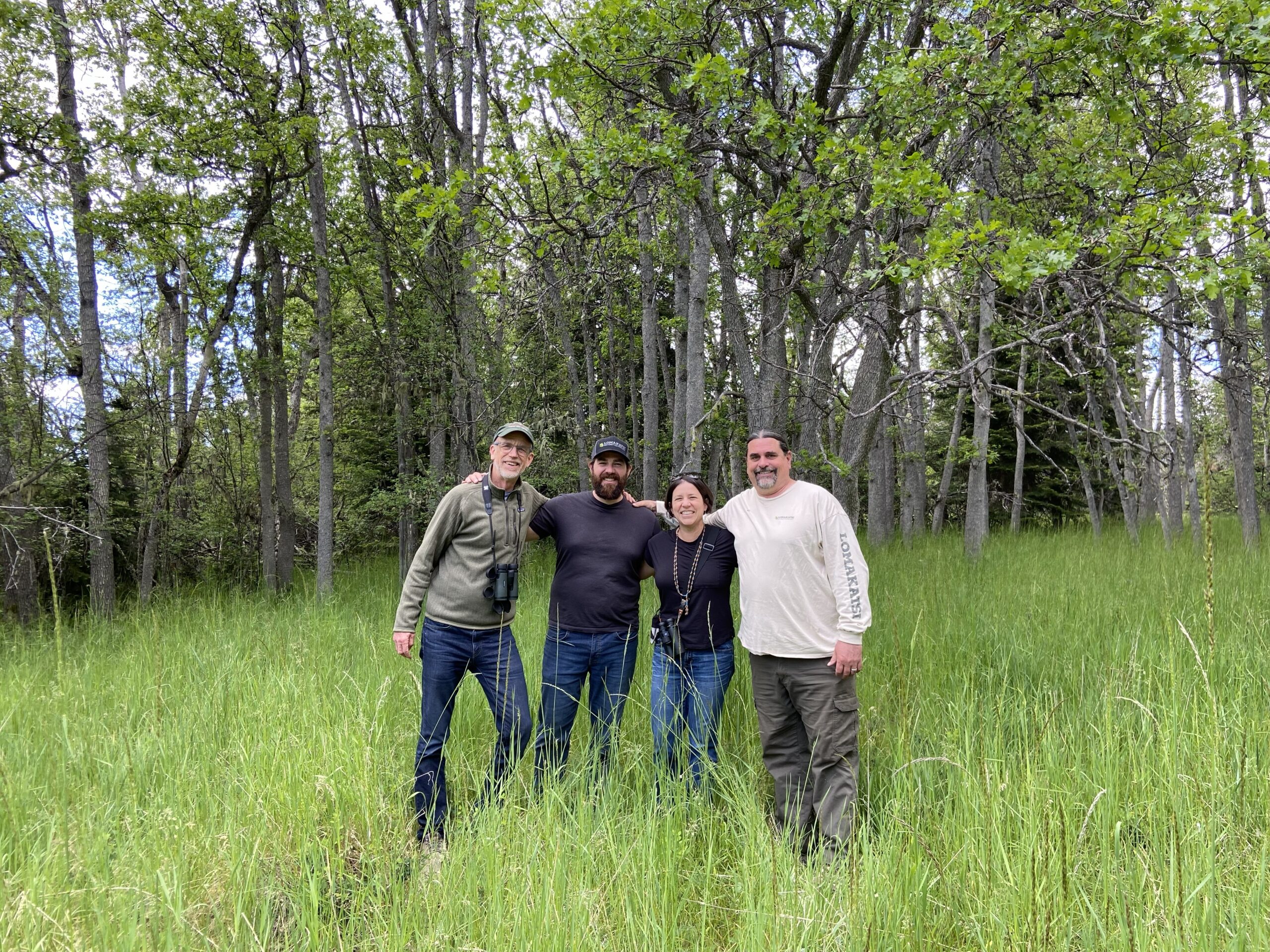 Three men and one woman stand together in an oak woodland, posing for a photo.