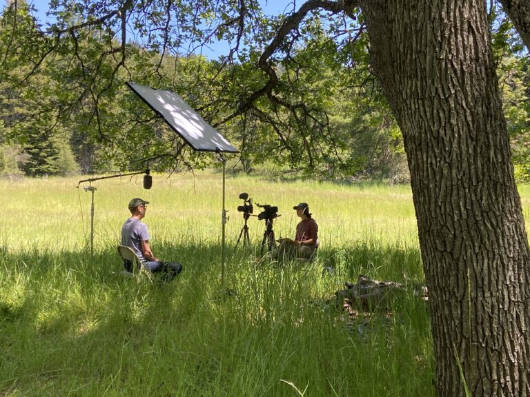 A woman interviews a man on film while they sit in an oak-prairie habitat.